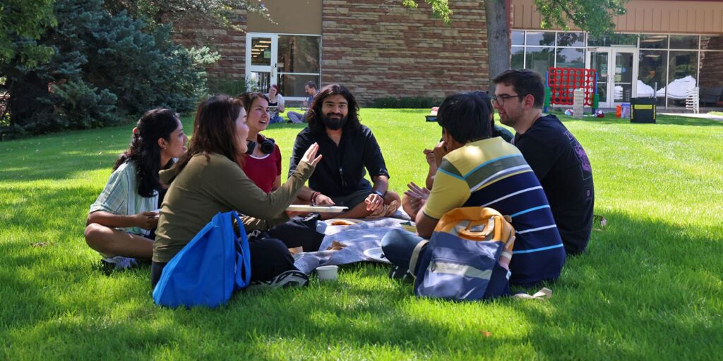 Graduate students sit in a circle in the grass.