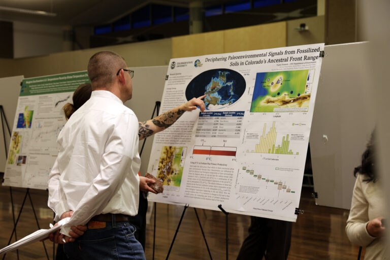 A person points to their poster at the GradShow.